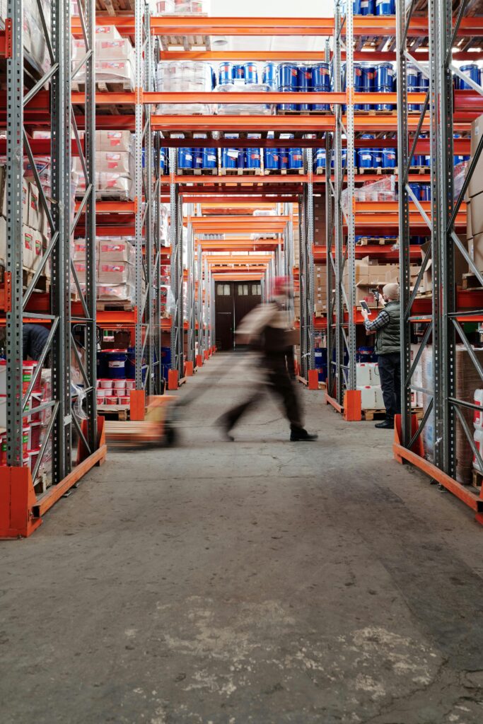 pexels-photo-4483859-4483859 Blurred motion of a man walking in a spacious warehouse aisle between tall shelves.
